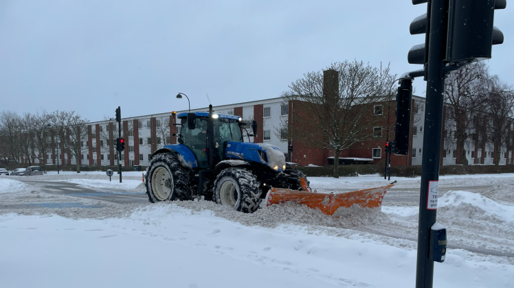 Blå traktor med sneplov rydder sne på en vej