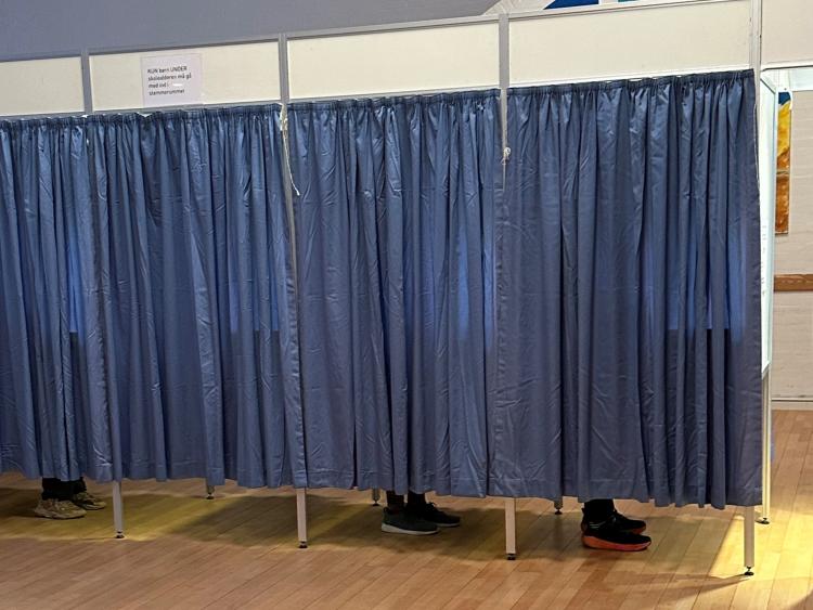 Stemmebokse med blå gardiner. Man kan se fødderne af vælgere, der er ved at stemme.