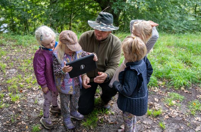 Børn og pædagog kigger på iPad i skoven