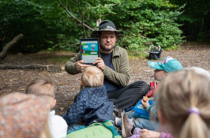 Pædagog viser børn iPad i skoven
