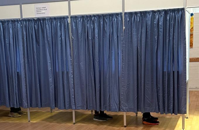 Stemmebokse med blå gardiner. Man kan se fødderne af vælgere, der er ved at stemme.